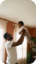 Father lifting his laughing baby into the air at home